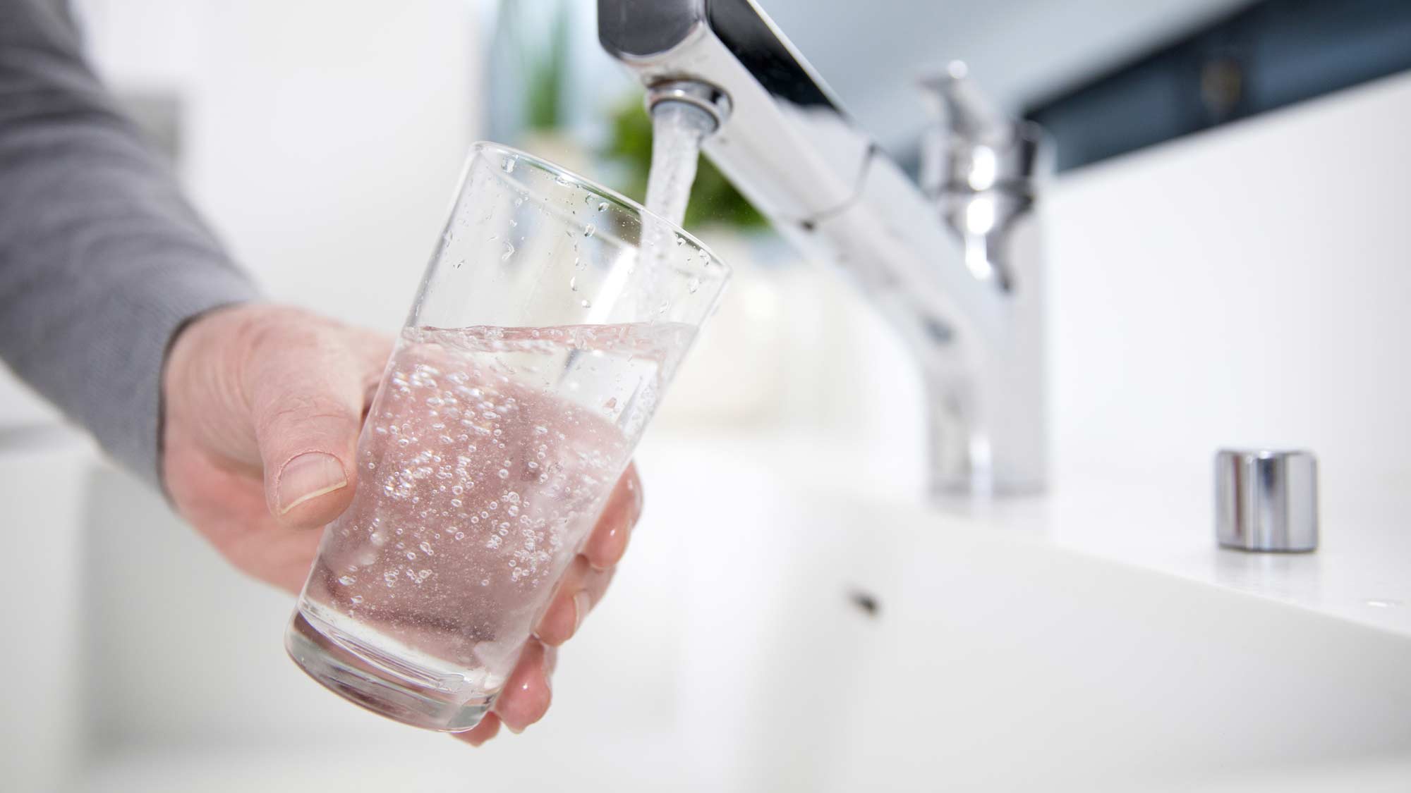 Person filling a glass of water from a kitchen faucet